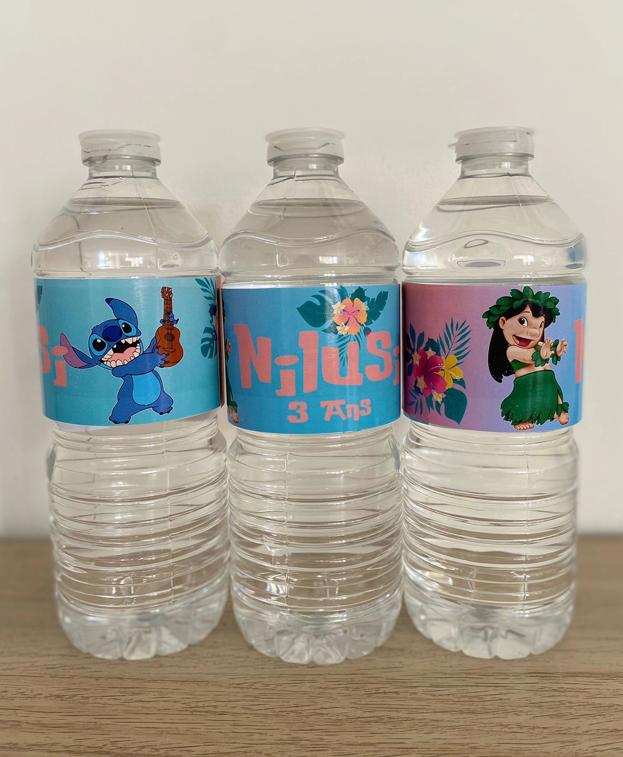 Trois grandes bouteilles d'eau personnalisées avec des étiquettes de Lilo et Stitch, incluant le nom Nilusi et l'inscription '3 ans'.