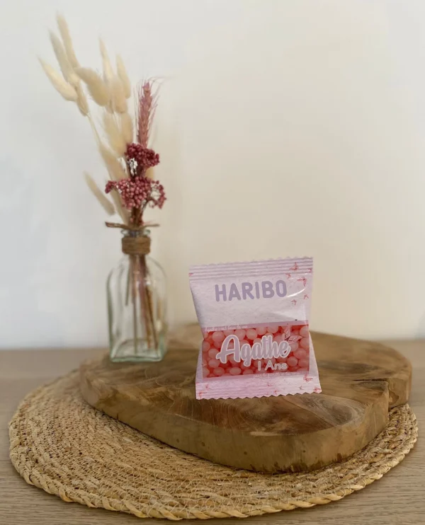 Sachet Haribo rose personnalisé avec le prénom Agathe et l'inscription '1 an', posé sur un support en bois.