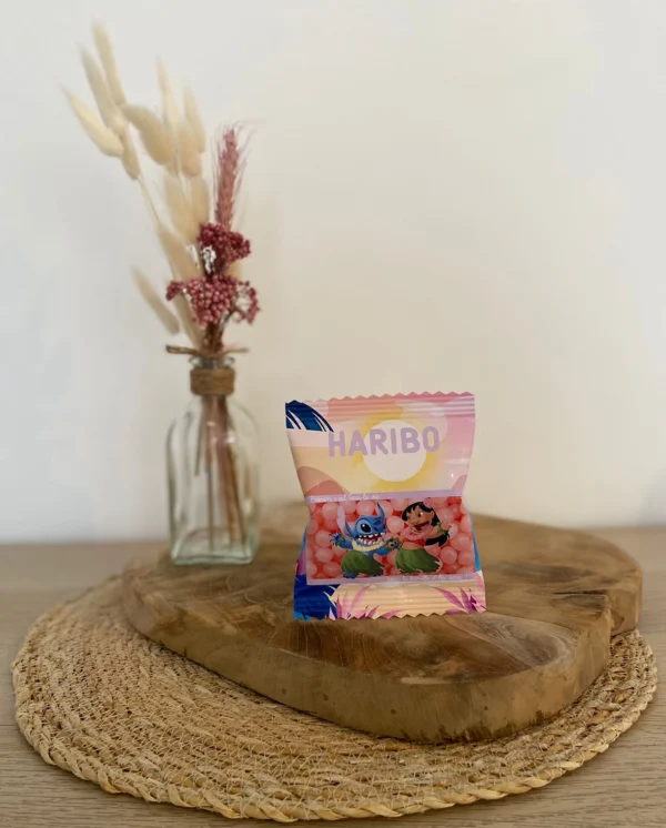 Sachet Haribo rose personnalisé avec des personnages de Lilo et Stitch, posé sur un support en bois.